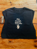 A black short-sleeve t-shirt with a white graphic print that reads 'PSA. The people pleaser has left the building' above a hand graphic, laid flat on a wooden surface.