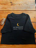 A black short-sleeve t-shirt with a graphic print on a wooden background. The graphic features a yellow crescent moon and the text 'MY PRONOUNS: WITCH / WITCHY' in white.